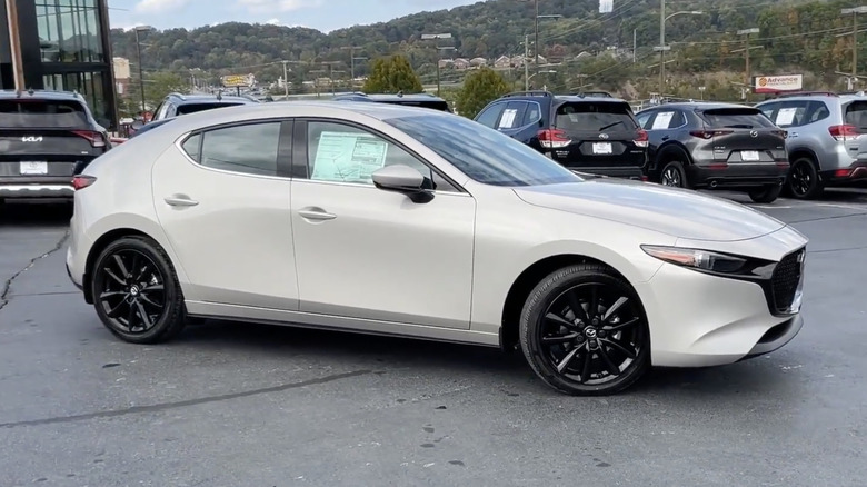 An off-white 2026 Mazda 3 in a dealerhsip parking lot against a mountainous backdrop