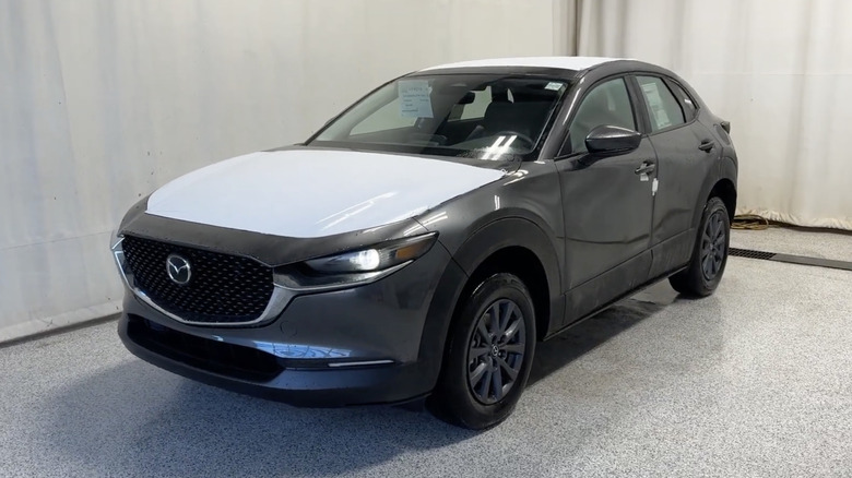 A dark gray 2026 Mazda CX-30 GX in a white showroom with protective plastic on its hood and roof