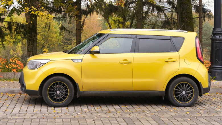 A yellow Kia Soul 2025 parked alongside a forest.