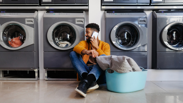 Young multiracial man in laundry, sitting on the floor, calling and waiting.