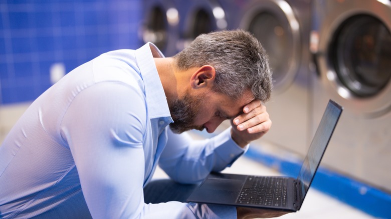 A man doing laundry while working on laptop.