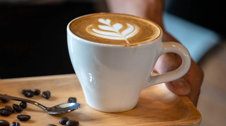 White ceramic cup of cappuccino with latte art held by barista