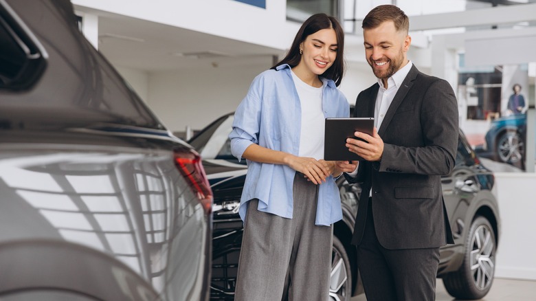Young woman looking at car salesman's tablet