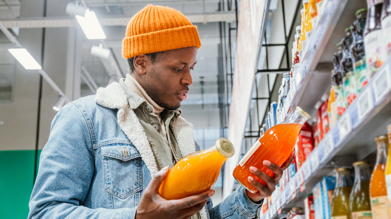 A man in a grocery store holding two juice containers comparing labels.
