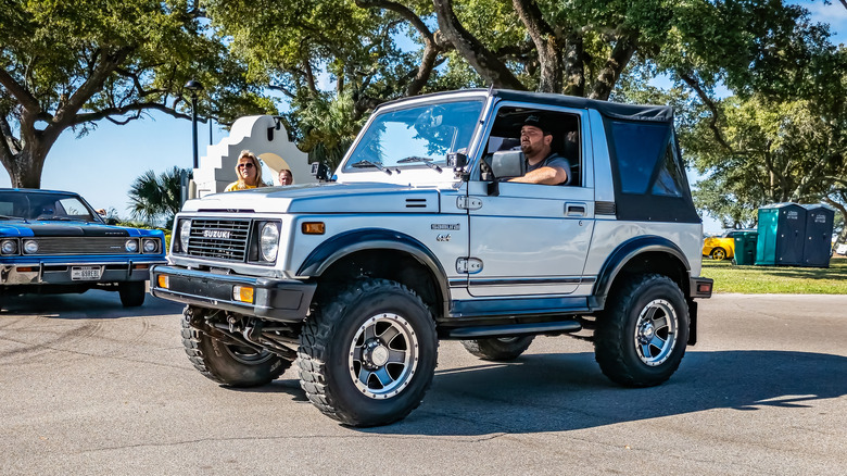 An ash 1988 Suzuki Samurai on a road with a man behind the wheel