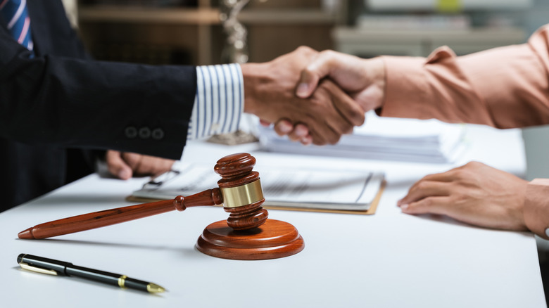 People shaking hands over a table with a pen and a gavel in the foreground.