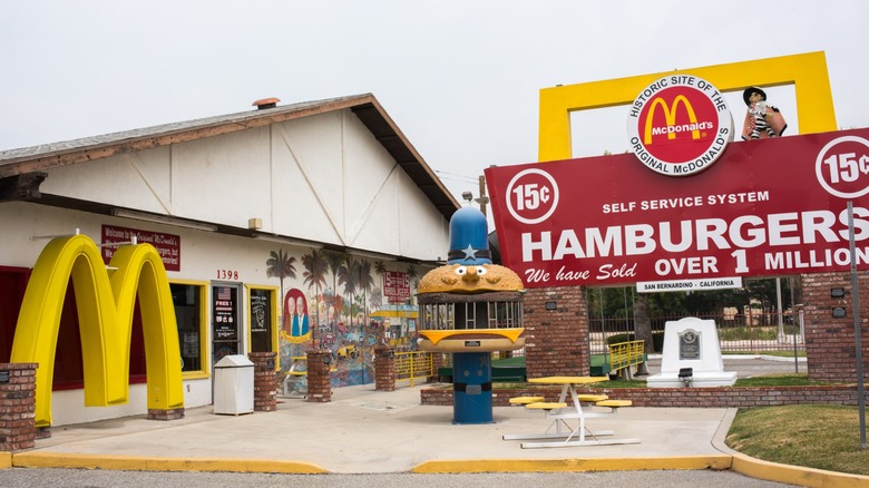 Exterior of the original McDonald's site museum in San Bernardino, with yellow arches, a giant vintage hamburger sign, and historic display features out front
