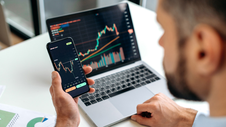 An overhead shot of a man trading on his phone and laptop.