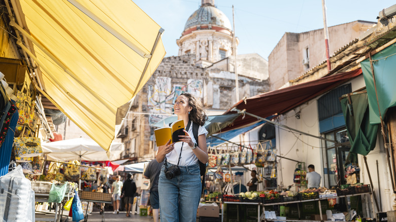A smiling young woman walking around Italy with a guide book.