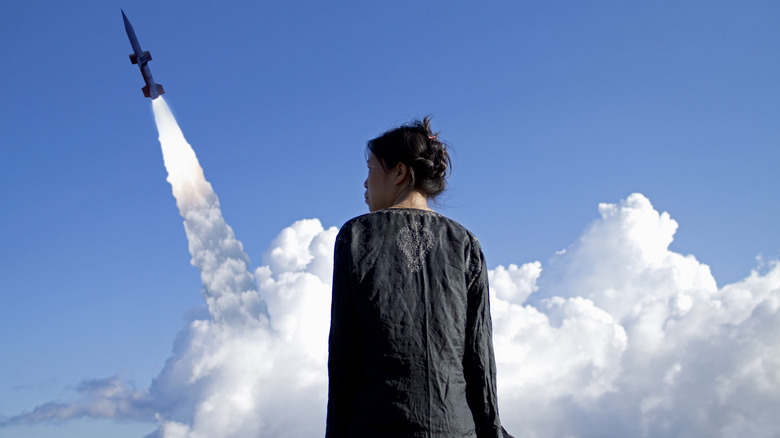 A woman with her back turned watching a missle launch.