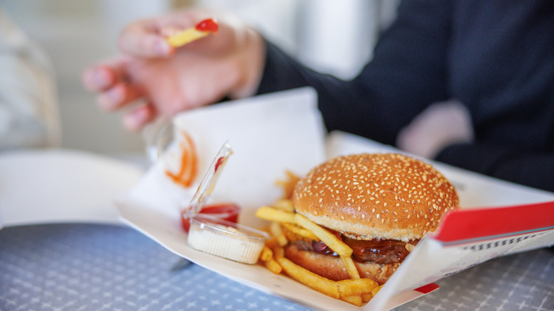 Person eating a fat food burger and fries