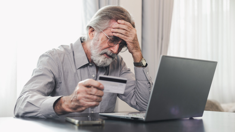 Older man infront of laptop holding a debit card.