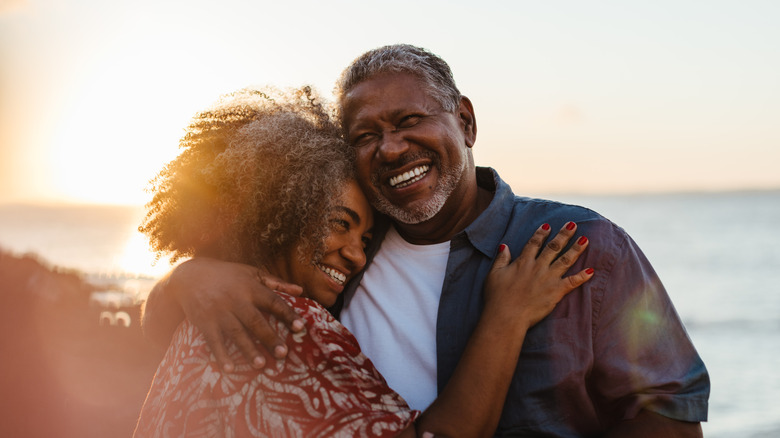 An older couple embracing on the beach with the sun setting behind them
