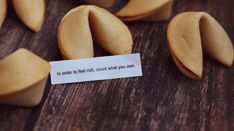 A group of fortune cookies on a table with one open to show a fortune talking about wealth.