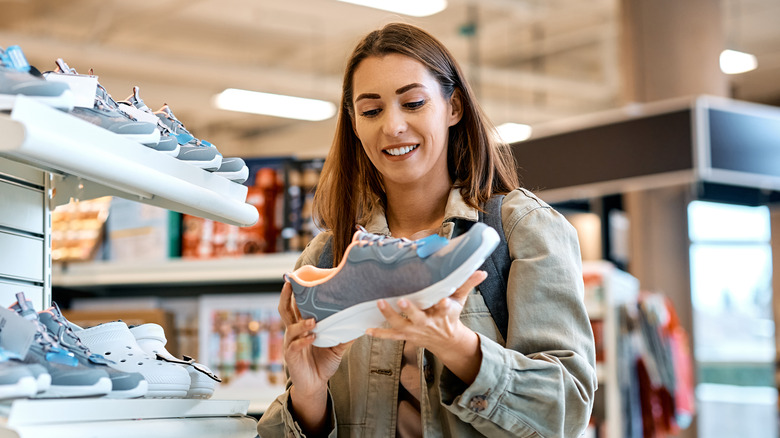 A woman in a shoe store smiling while holding a sneaker.