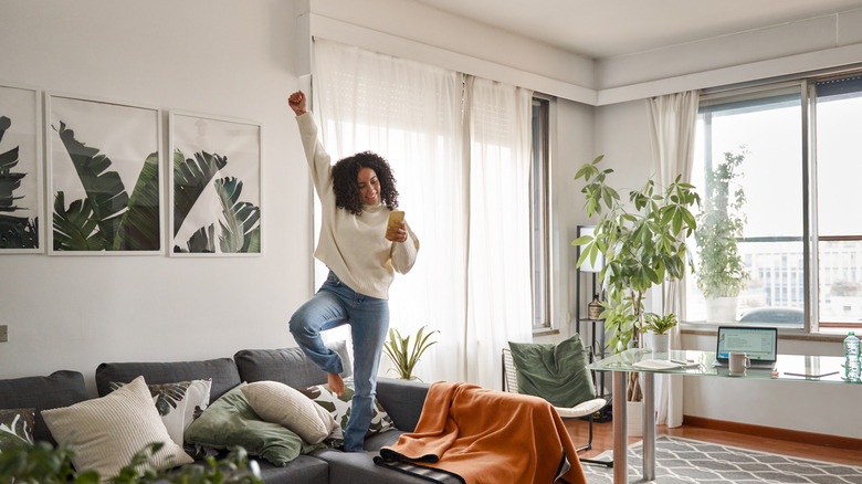 Happy excited young woman using smartphone dancing at home.