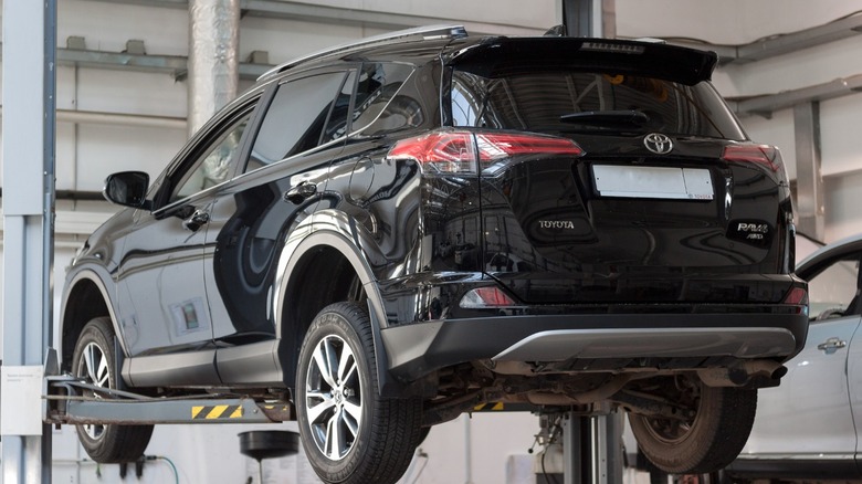 Black Toyota RAV4 raised on a lift in an auto repair shop, viewed from the rear