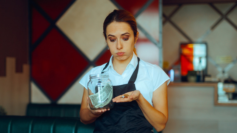 A server&nbsp;looking disappointed as she holds a tip jar