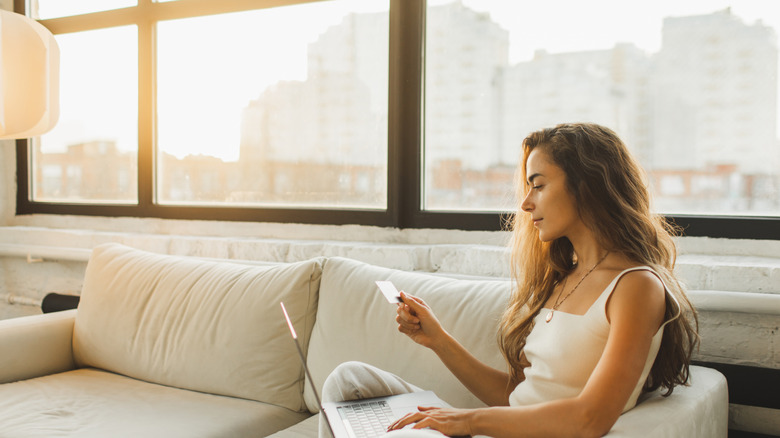 Woman on a couch using a credit card on her laptop