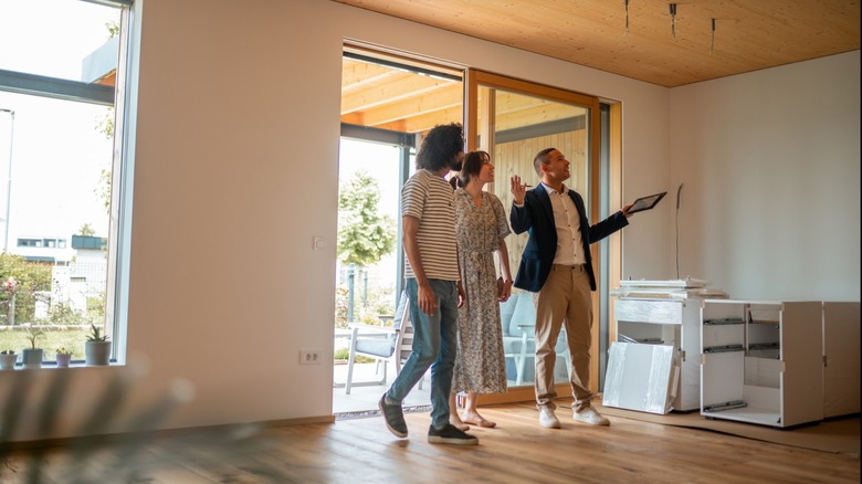 Real estate agent showing a couple around a bright, modern home with large windows and wooden floors