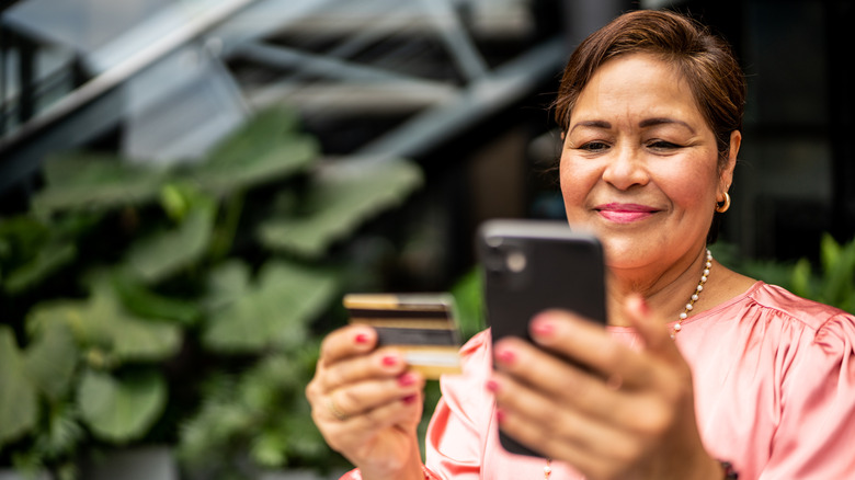 A mature woman looking at phone and credit card.