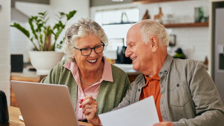 A retired couple sitting in their home in front of a computer discussing retirement plans.