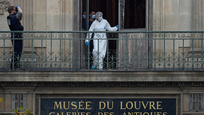 A forensic investigator examines a broken window at the Louvre in Paris while being photographed by a police photographer.
