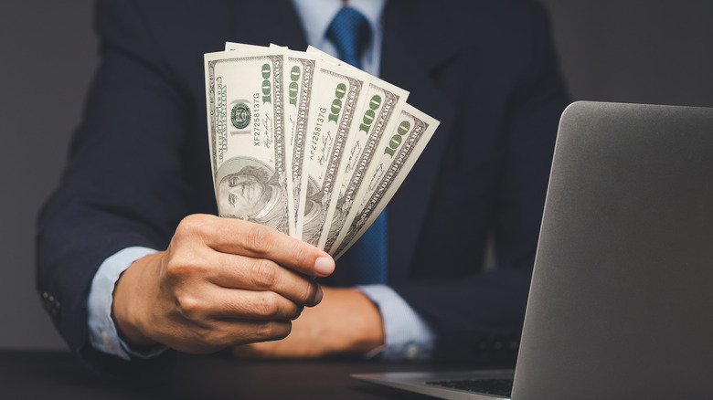 Confident businessman showing cash near laptop.