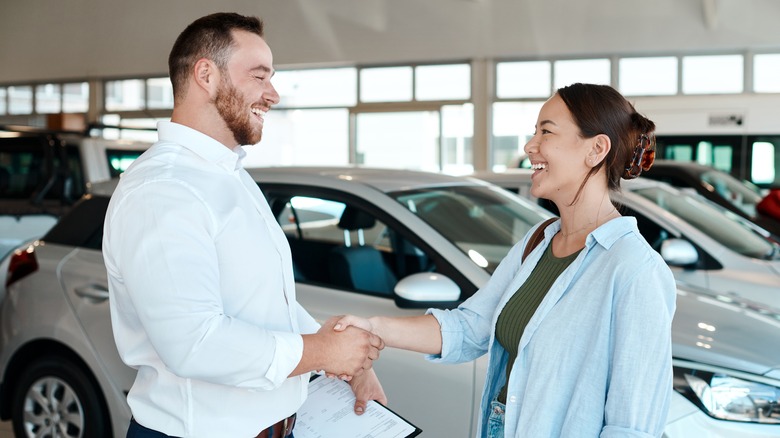 A happy woman shaking hands with another happy man while a vehicle is in the background