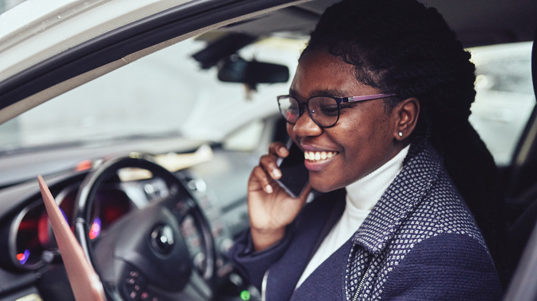 A young woman is sitting in a car with a laptop and working or studying online.