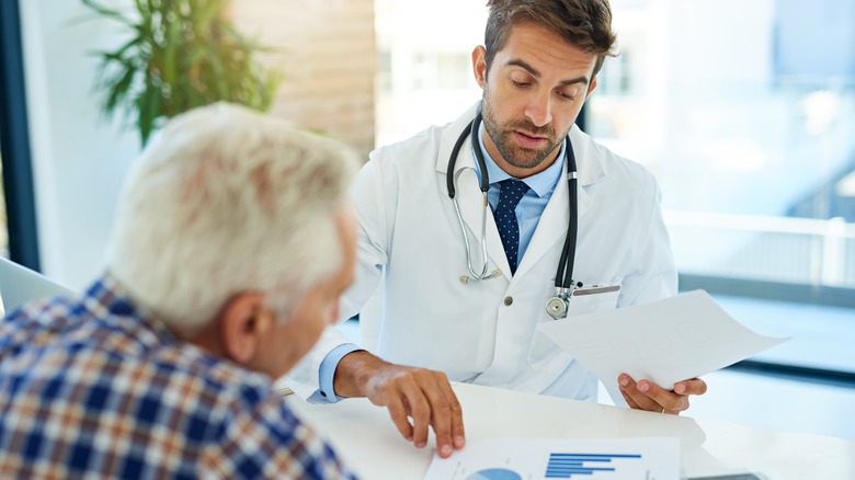 Male doctor and old man sit at table discussing documents