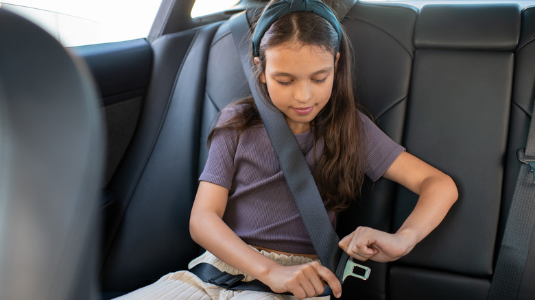 A little girl adjusting her seatbelt.