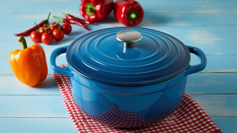 An orange Le Creauet dutch oven, surrounded by asparagus, garlic, spoon, and pepper grinder