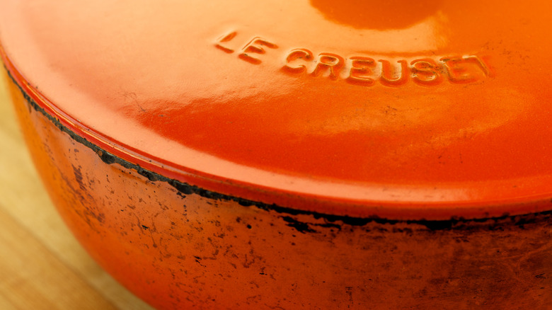 An orange Flame Le Creuset dutch oven with evidence of heavy cooking on pot sides