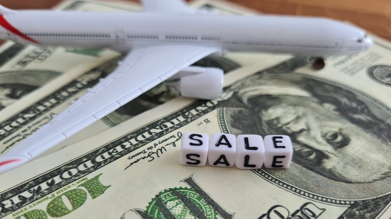 Toy plane on top of money with beads reading "sale"