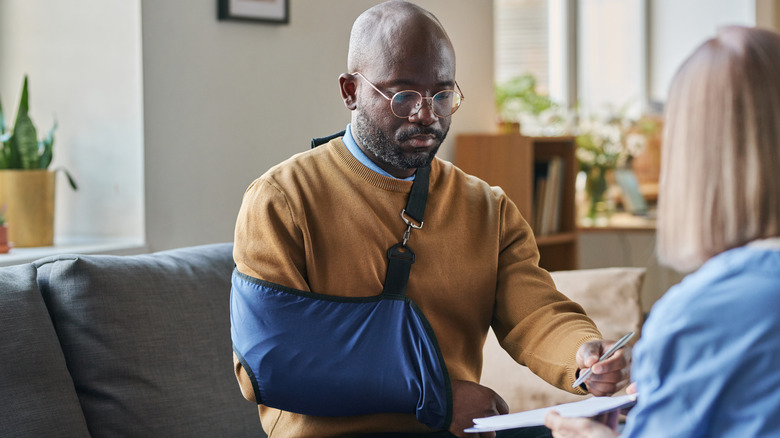 A man with his arm in a sling signing a bill