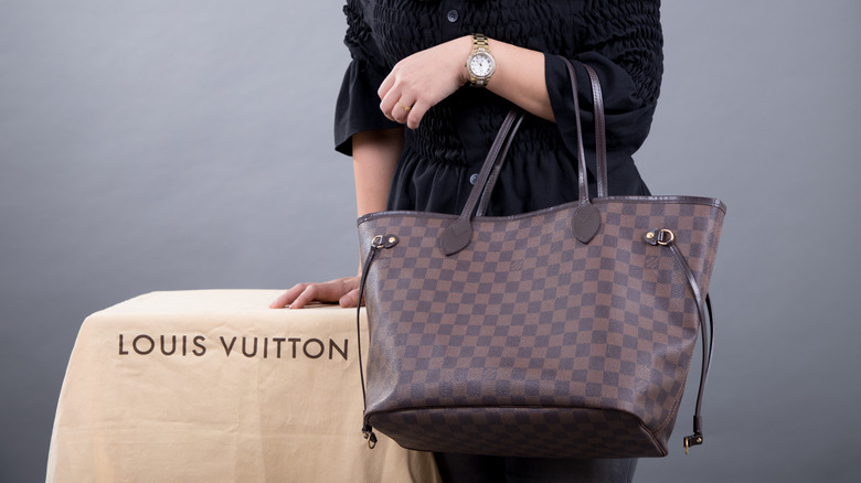 Woman with Louis Vuitton bag Neverfull size mm Damier style in studio.