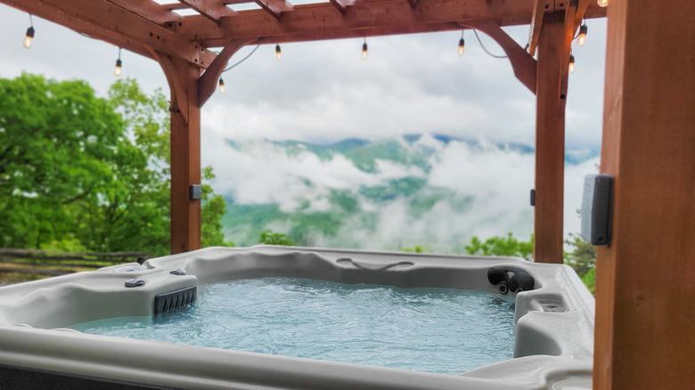 A large hot tub on a window deck, under a lit gazebo, with a Smoky Mountain view
