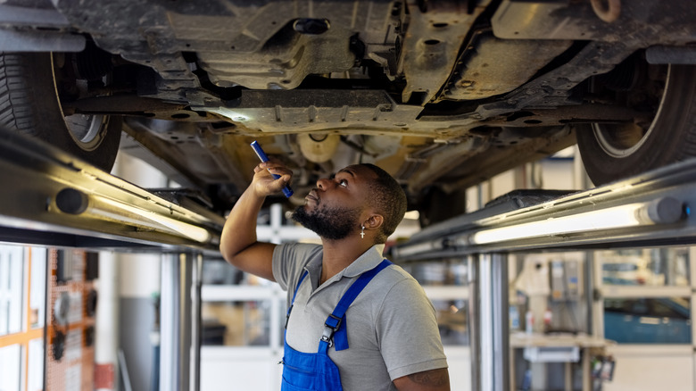 Repair man inspecting underneath a car with light