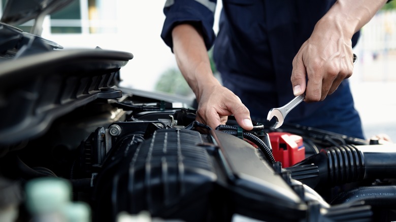 Hands of a car mechanic with wrench working on engine