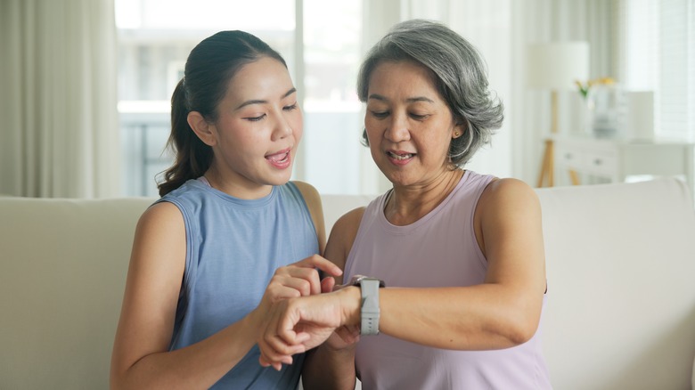 Young adult child give gift AI smart watch IOT app to mature middle age old mum.