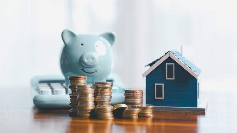 Stack of couns alonh with a toy house, piggy bank, and calcuator.