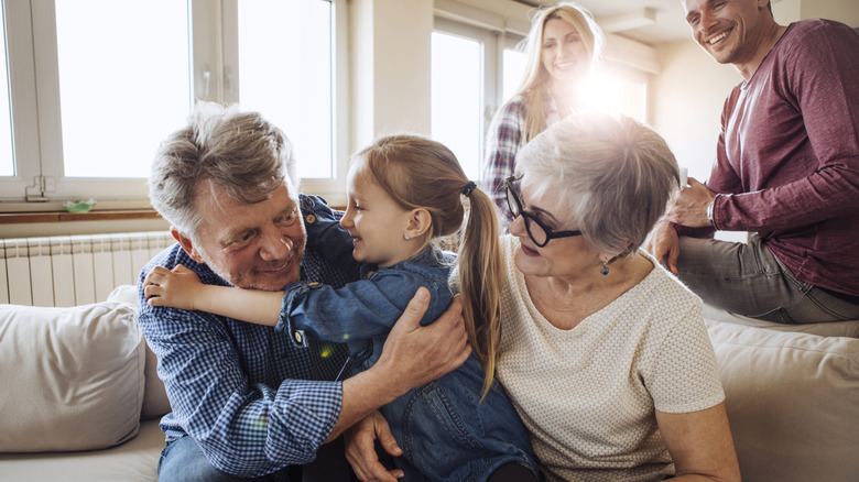 Family gathering at sofa, with grandparents hugging their grandchild