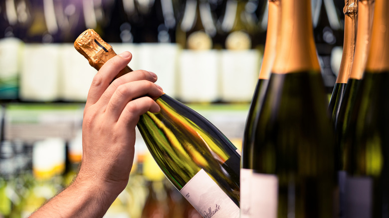 A male-presenting hands takes a glass wine bottle off a shelf in a liquor store