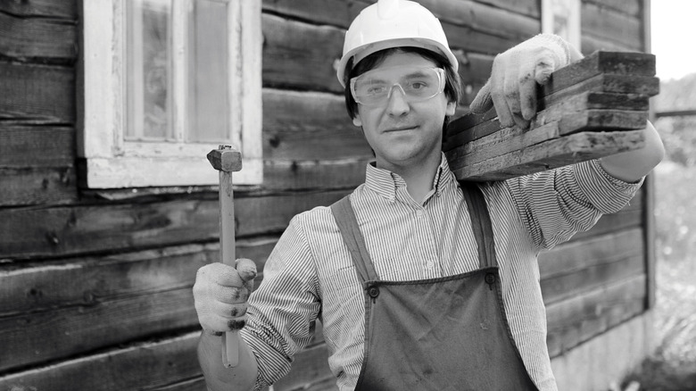 worker holding boards and a hammer on a jobsite
