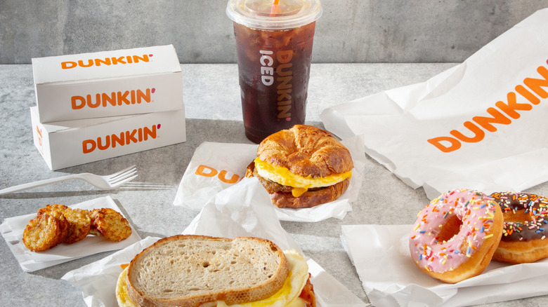 A collection of Dunkin' Donuts food and drink items including an egg sandwich, donuts, iced coffee, and hash browns.