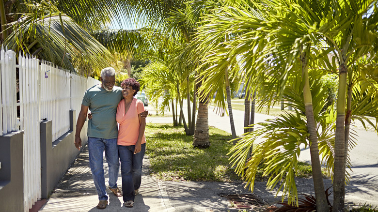 An older African American couple walking on a sidewalk with palm trees in Flordia