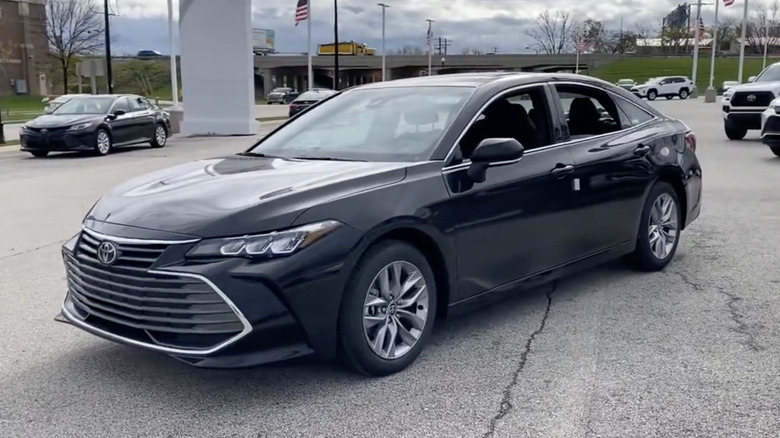 A black 2022 Toyota Avalon in a dealership parking lot with its windows rolled down