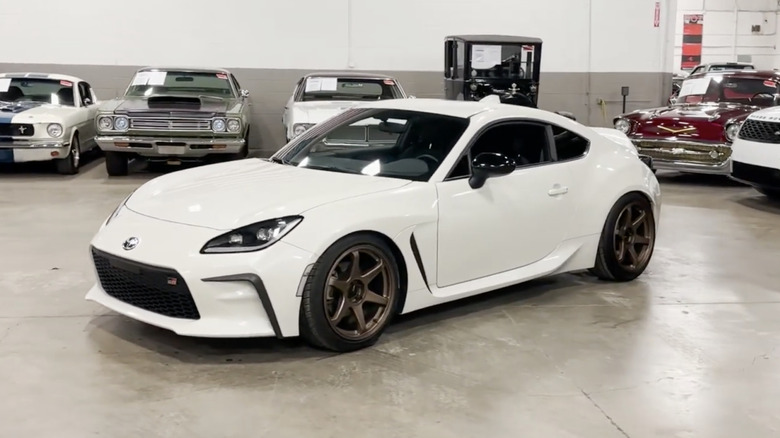 A white 2022 Toyota GR86 parked in a garage in front of a line of classic cars