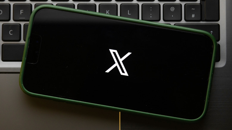 The X logo on a phone screen, which is on top of a laptop's keyboard.